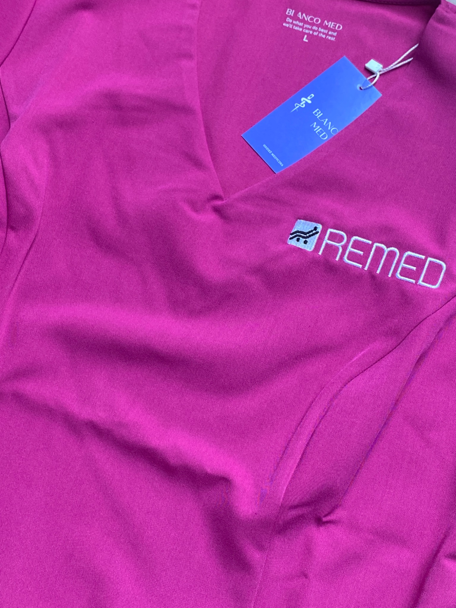 Fuksjowa bluza medyczna Blanco Med z haftowanym logo Remed, widoczna metka i rozmiar L. Uniform dla fizjoterapeutów, komfort i trwałość w pracy.