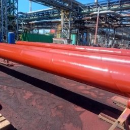 TOPREM SPÓŁKA Z OGRANICZONĄ ODPOWIEDZIALNOŚCIĄ - Czerwone rury przemysłowe po malowaniu na tle konstrukcji stalowej w fabryce. Widoczne spawy i połączenia.