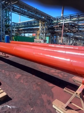 Czerwone rury przemysłowe po malowaniu na tle konstrukcji stalowej w fabryce. Widoczne spawy i połączenia.