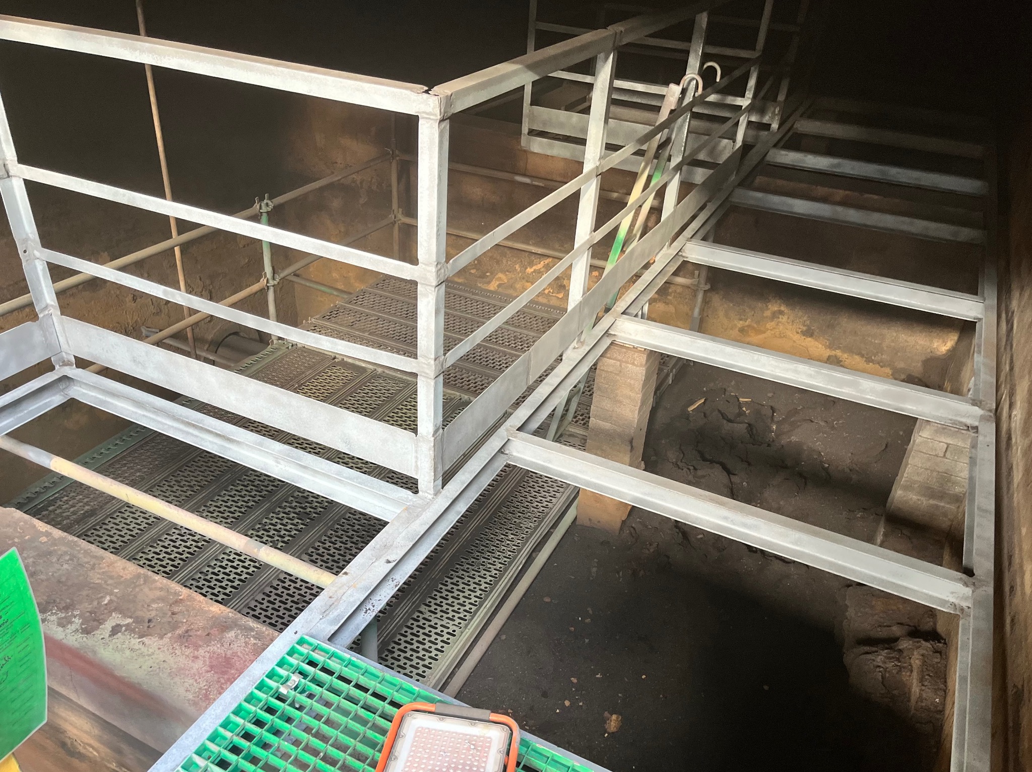 Metalowa konstrukcja rusztowania wewnątrz ciemnego, przemysłowego zbiornika. Widoczne metalowe kraty i fragmenty ścian zbiornika z osadami.