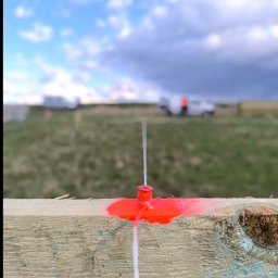 PERFECT-GEO Usługi geodezyjne Jakub Szczeblewski - Czerwony kołek z linką na drewnianej desce, w tle łąka i niebo. Wyznaczanie terenu.