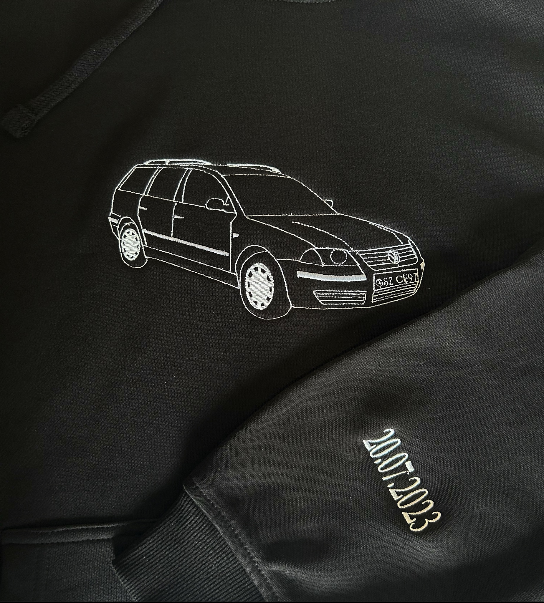 Czarna bluza z kapturem, haftowany biały kontur samochodu i data na rękawie. Detal wykonany w Sztum.