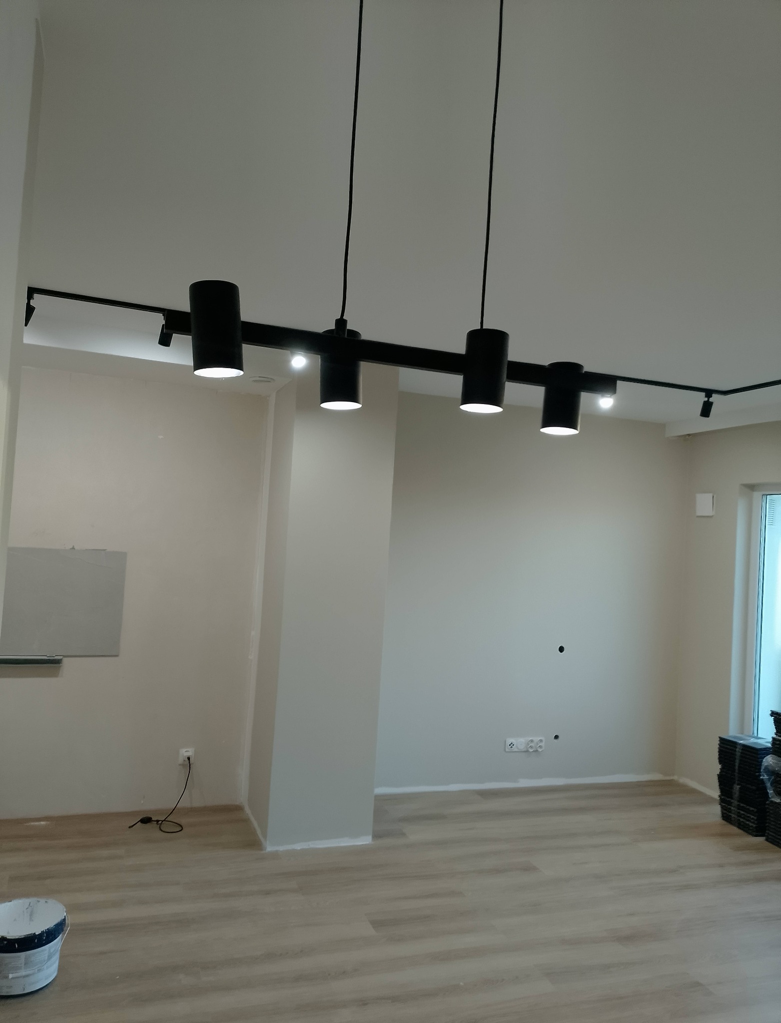 Nowoczesne oświetlenie sufitowe z czarnymi reflektorami w wykończonym wnętrzu. Widoczne gładkie ściany w odcieniach beżu i panele podłogowe. Minimalistyczny design.