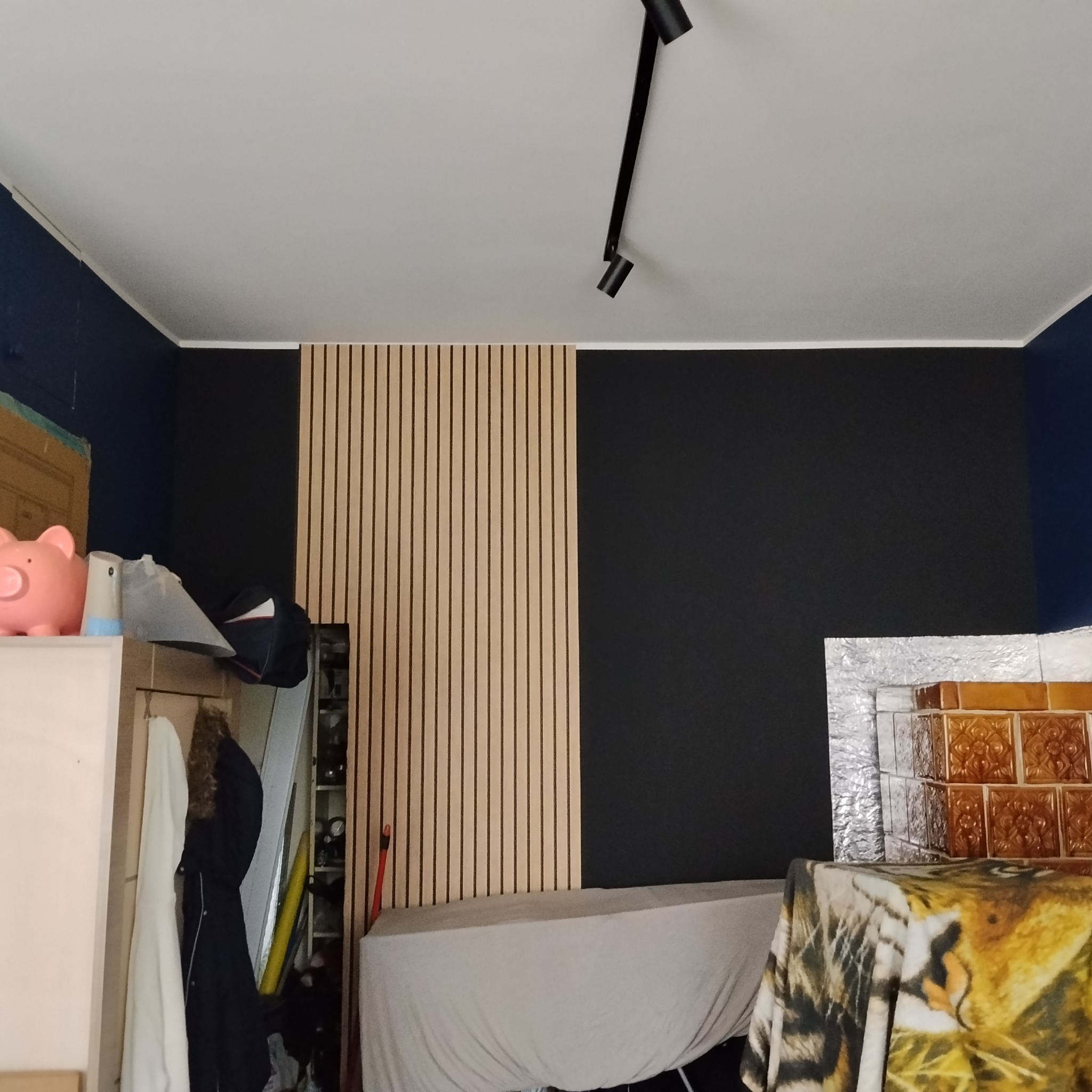 Częściowy widok pokoju po wykończeniu: czarna ściana, drewniane panele pionowe, oświetlenie punktowe. W tle widoczny piec kaflowy.