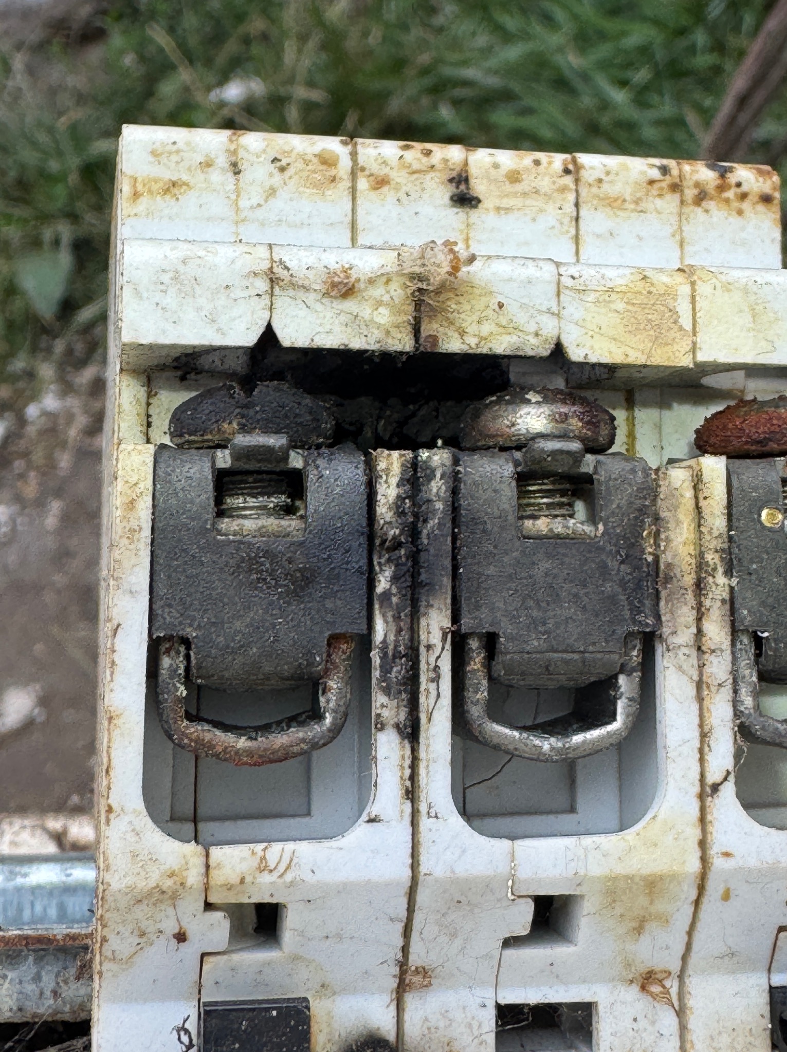 Przepalony, stary bezpiecznik elektryczny z widocznymi śladami zwarcia i nadpaleniami, zardzewiałe elementy metalowe, brudna obudowa, z bliska.