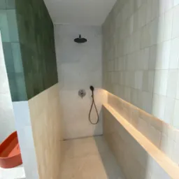 Nowoczesna kabina prysznicowa z zielonymi i beżowymi płytkami, deszczownicą i podświetleniem LED. Minimalistyczny design z umywalką w odcieniach terakoty.