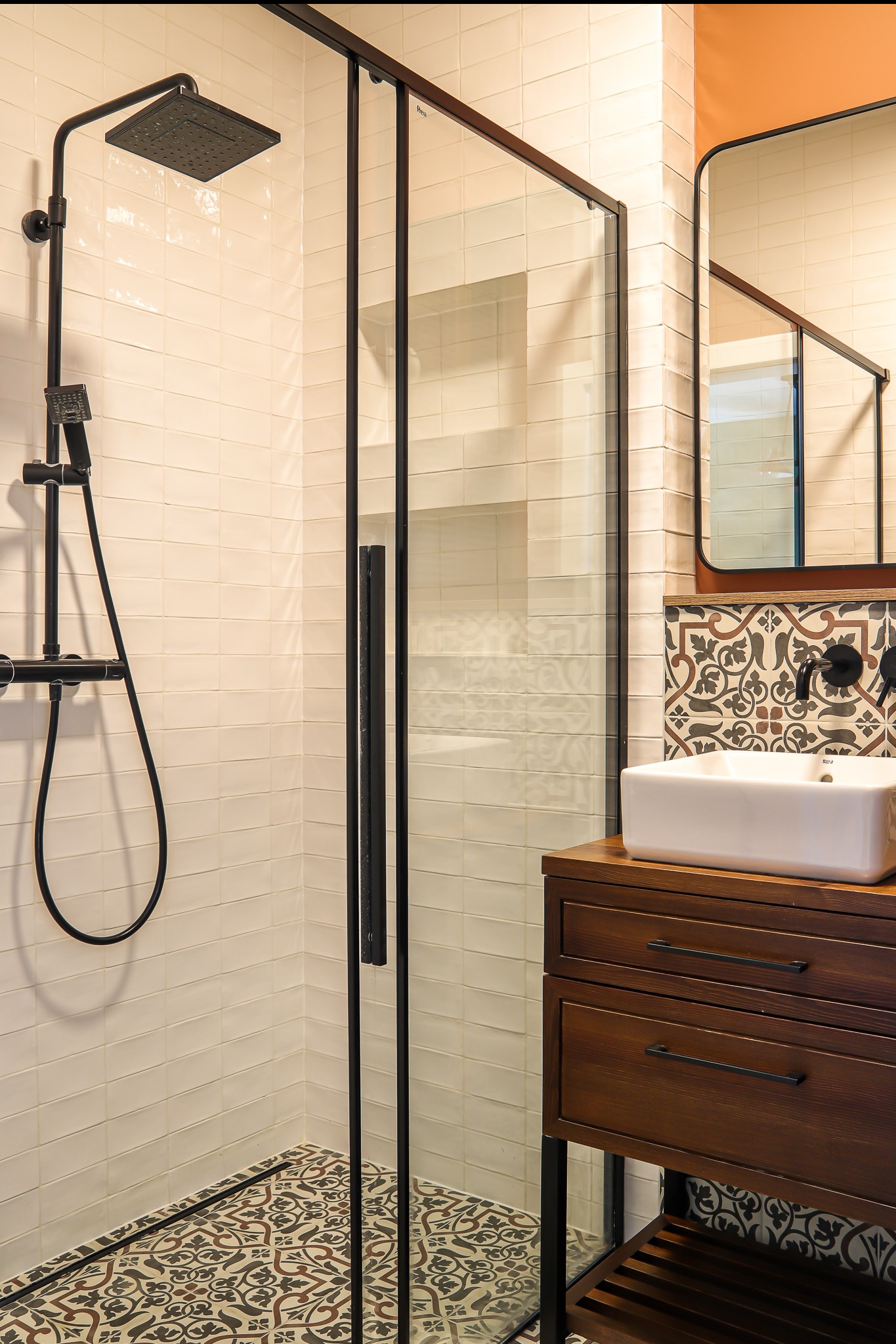 Nowoczesna łazienka z kabiną prysznicową typu walk-in, białą umywalką nablatową na drewnianej szafce i wzorzystą glazurą podłogową.