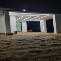 Nowoczesny dom z oświetleniem LED na zewnątrz, nocą. Nietypowy układ lamp w kształcie zygzaka. Widoczne narzędzia pracy.