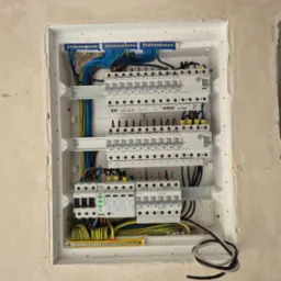 Rozdzielnia elektryczna wnękowa z zainstalowanymi zabezpieczeniami, przewodami i listwami, umieszczona w surowej ścianie, gotowa do podłączenia.