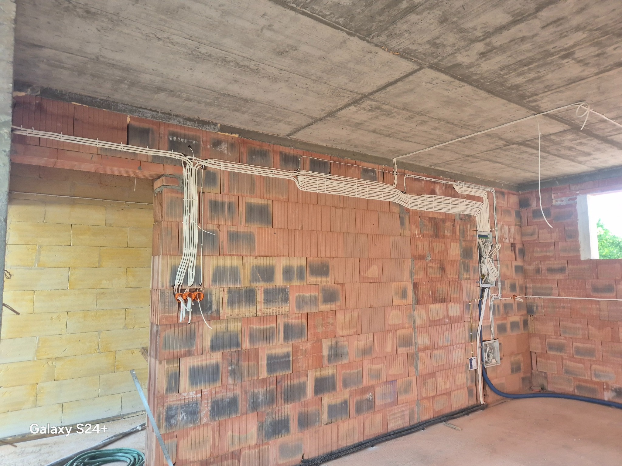 Wnętrze w trakcie budowy z widoczną instalacją elektryczną: przewody ułożone wzdłuż ceglanej ściany i pod sufitem. Widoczne puszki i peszle.
