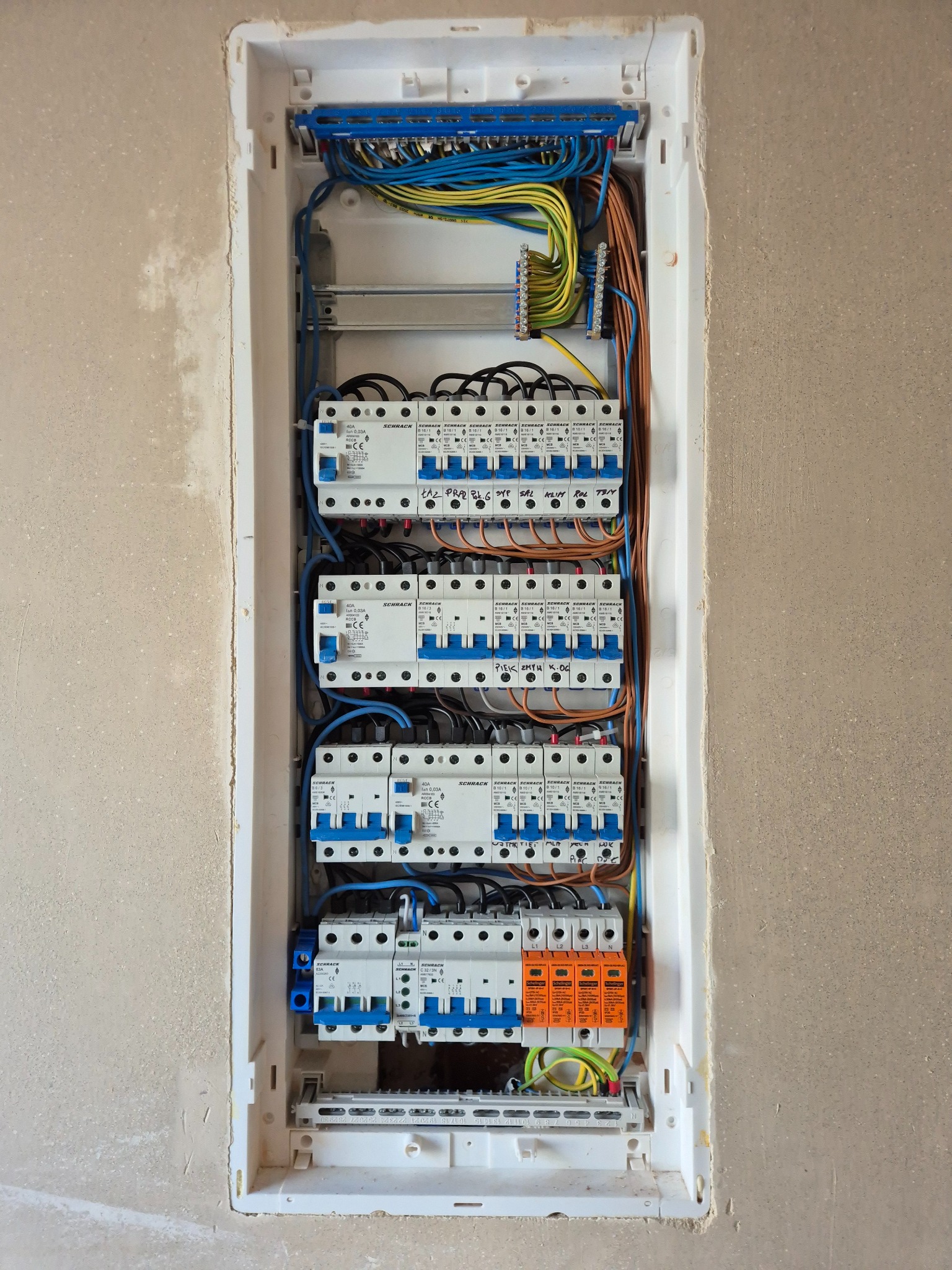 Rozdzielnica elektryczna z zabezpieczeniami różnicowoprądowymi i nadprądowymi, okablowana przewodami w kolorach: żółtym, niebieskim, brązowym, czarnym i zielono-żółtym.