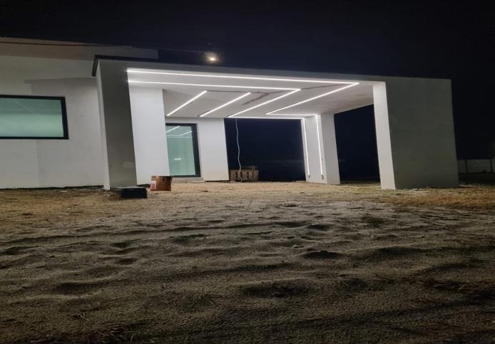 Nowoczesny dom z oświetleniem LED na zewnątrz, nocą. Nietypowy układ lamp w kształcie zygzaka. Widoczne narzędzia pracy.