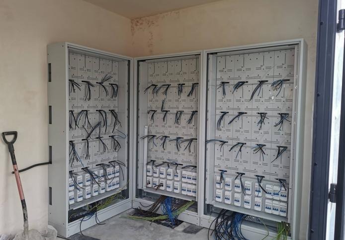 Rozdzielnia elektryczna z licznymi zabezpieczeniami i przewodami, częściowo zamontowana w surowym wnętrzu. Widoczna łopata. Instalacja w trakcie prac.