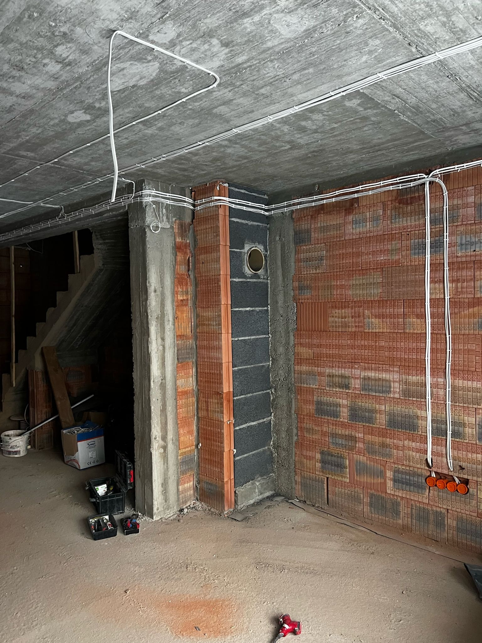 Instalacja elektryczna w surowym wnętrzu: białe kable prowadzone po suficie i ścianach z cegły dziurawki, puszki elektryczne w ścianie. Widoczne narzędzia.