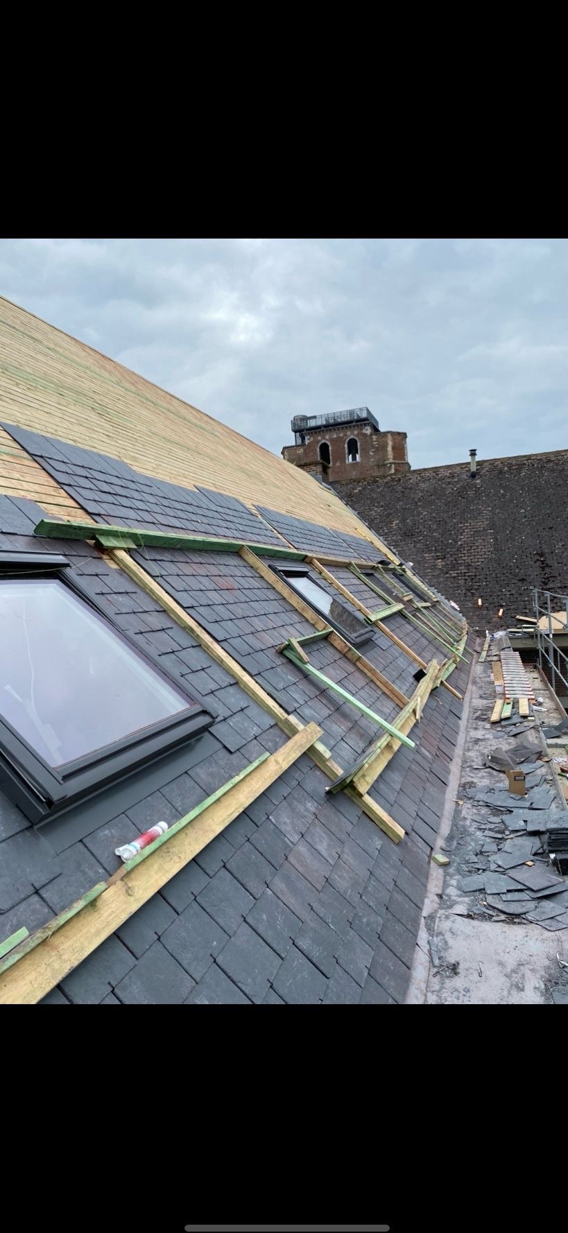 Montaż dachówki na połaci dachu z oknami. W tle widoczna wieża. Fragment rusztowania. Dach pokryty częściowo membraną.