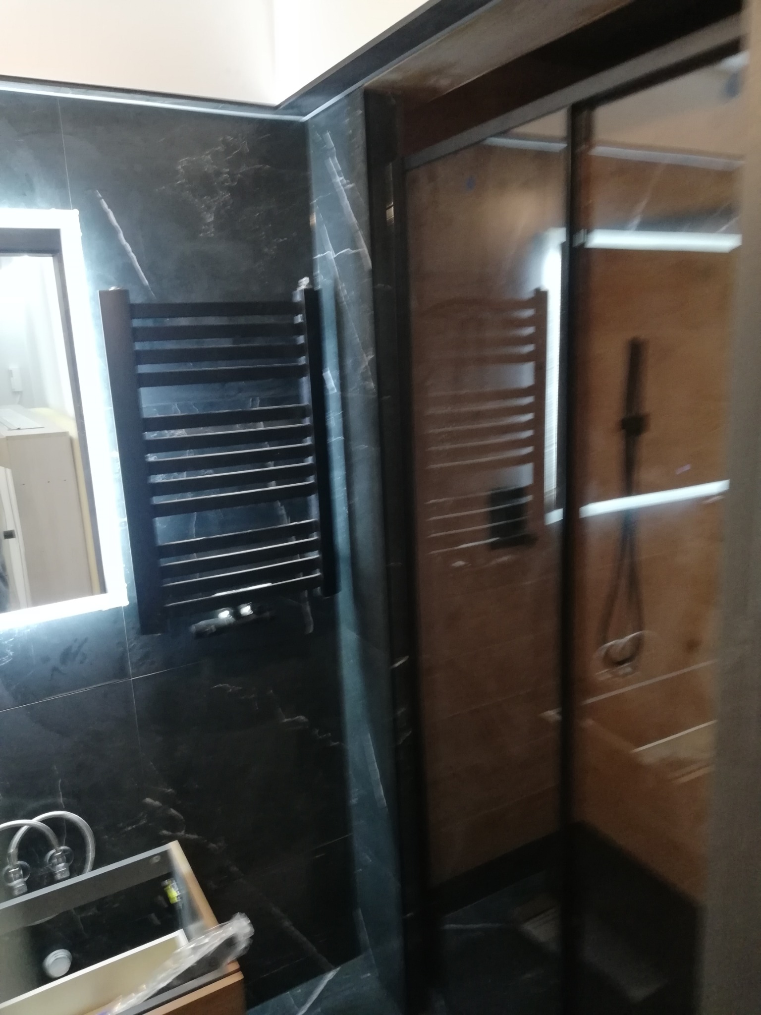 Wykończona łazienka z czarnymi płytkami imitującymi marmur, grzejnikiem drabinkowym i kabiną prysznicową z ciemną ramą. Widoczna umywalka z baterią.