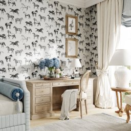 Mala & Co. Malwina Wilczek - Jasny pokój z biurkiem i tapetą w konie. Biurko z szufladami, krzesło z narzutą, okno z zasłoną. Na biurku wazon z kwiatami. Dwa obrazy na ścianie.