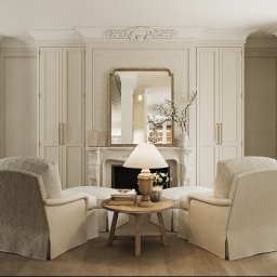 Mala & Co. Malwina Wilczek - Elegancki salon w kremowych barwach z kominkiem, lustrem i dwoma fotelami. Klasyczny wystrój wnętrza z dbałością o detale i symetrię.
