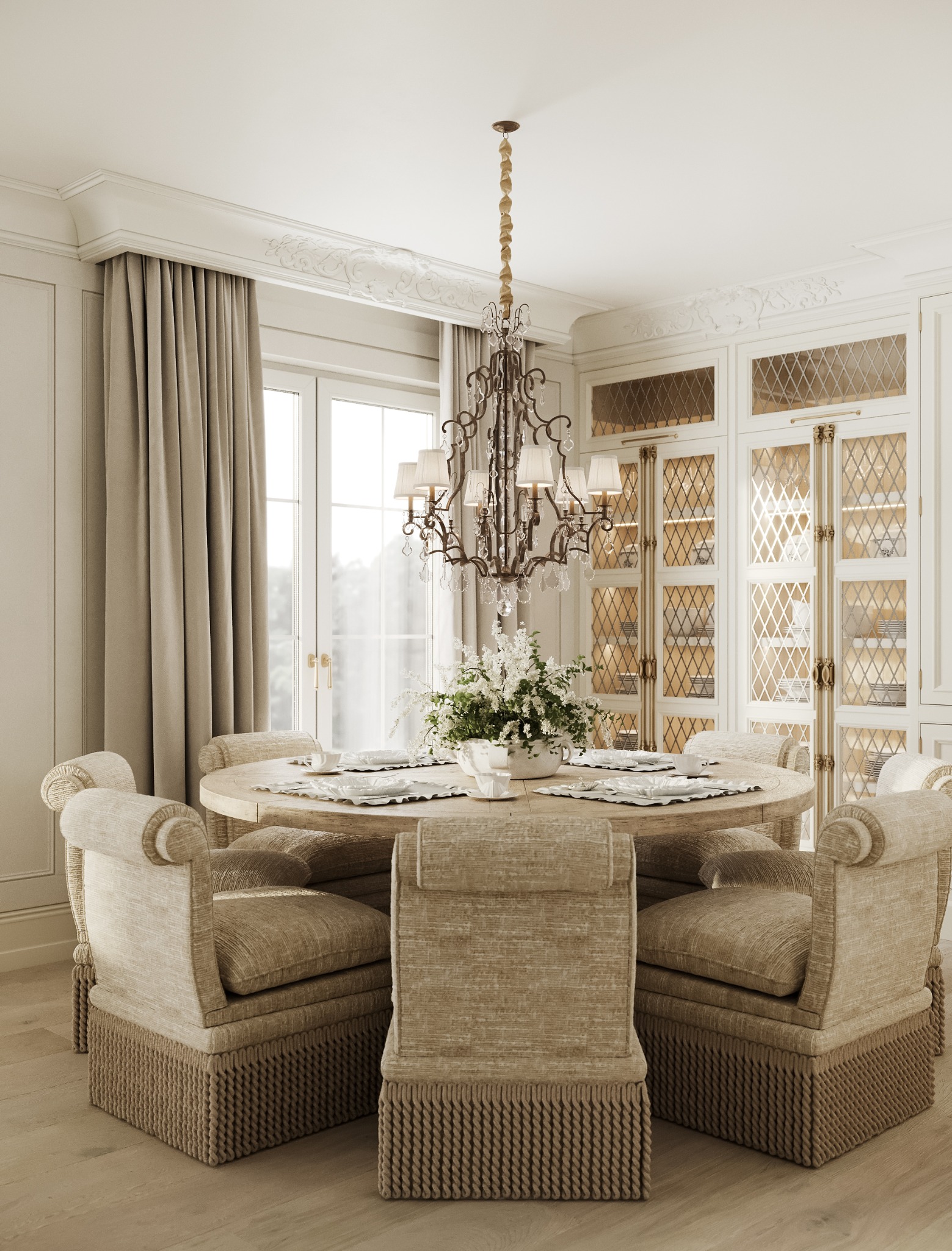 Jadalnia w stylu klasycznym: okrągły stół z kwiatami, krzesła z frędzlami, żyrandol z kryształkami, przeszklona witryna. Stonowana kolorystyka, elegancki wystrój.