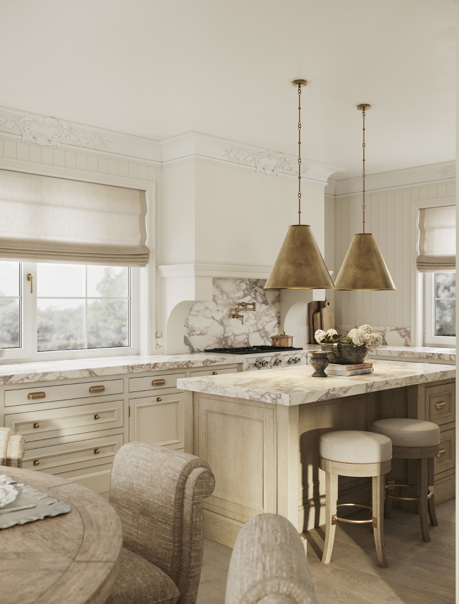 Elegancka kuchnia w stylu klasycznym: marmurowy blat, kremowe szafki z mosiężnymi uchwytami, zwisające lampy i dekoracyjne sztukaterie. Dwa hokery przy wyspie.