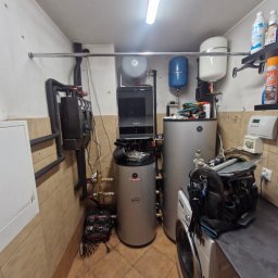 FJ Instal Jakub Furczyk - Dwa srebrne bojlery Termica Inox w kotłowni, obok pralka, narzędzia i instalacja CO. Widoczne rury, zawory i czujniki. Oświetlenie jarzeniowe.