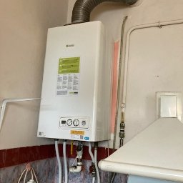 3CE Karol Lange - Biały piec gazowy Beretta z podłączonymi rurami, zamontowany na ścianie w pomieszczeniu z okapem i płytkami. Widoczny przewód kominowy.