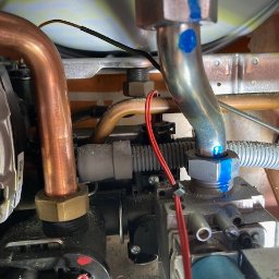 3CE Karol Lange - Wnętrze kotła gazowego z miedzianymi rurami i zaworami, widoczne przewody elektryczne i elementy instalacji. Detal z niebieskimi oznaczeniami na metalowych złączkach.