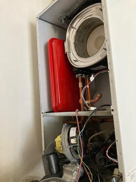 Wnętrze kotła gazowego z widocznymi elementami instalacji, zbiornikiem wyrównawczym i podzespołami. Widok z bliska na komponenty wewnątrz obudowy.