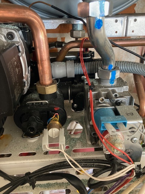 Wnętrze pieca gazowego z widocznymi miedzianymi rurami, elementami elektrycznymi i drobnymi zanieczyszczeniami. Ujęcie z bliska, ukazujące detale instalacji.