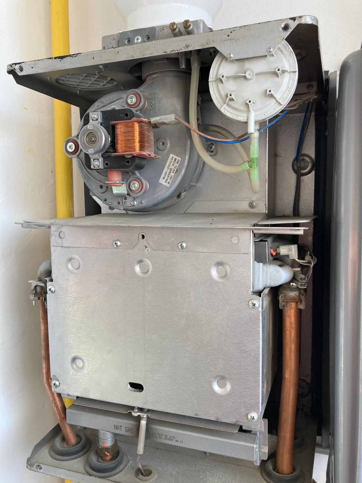 Otwarty piec gazowy z widocznymi elementami wewnętrznymi, w tym cewką i rurami miedzianymi. Usługi gazownicze w Gdyni. Widok z bliska na wnętrze urządzenia.