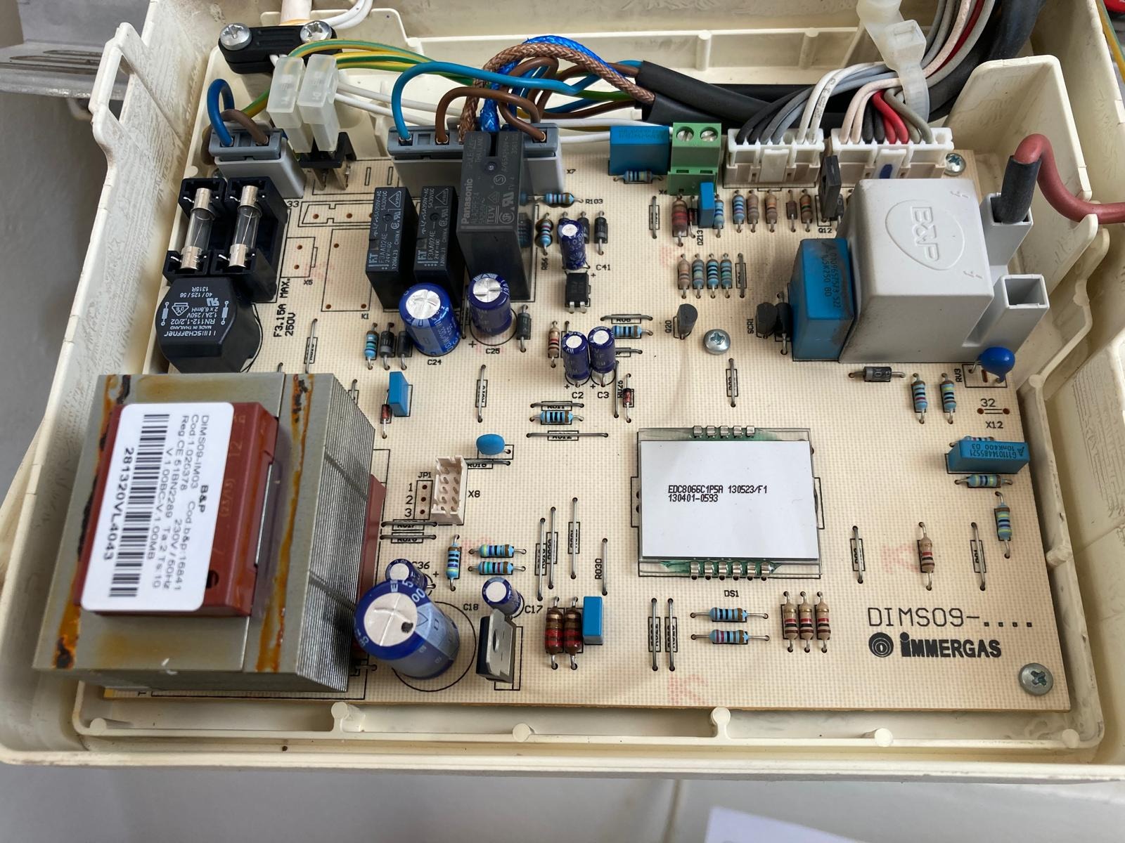 Wnętrze obudowy pieca gazowego Immergas z widoczną płytą sterującą, elementami elektronicznymi i okablowaniem. Widoczne kondensatory, rezystory i transformator.