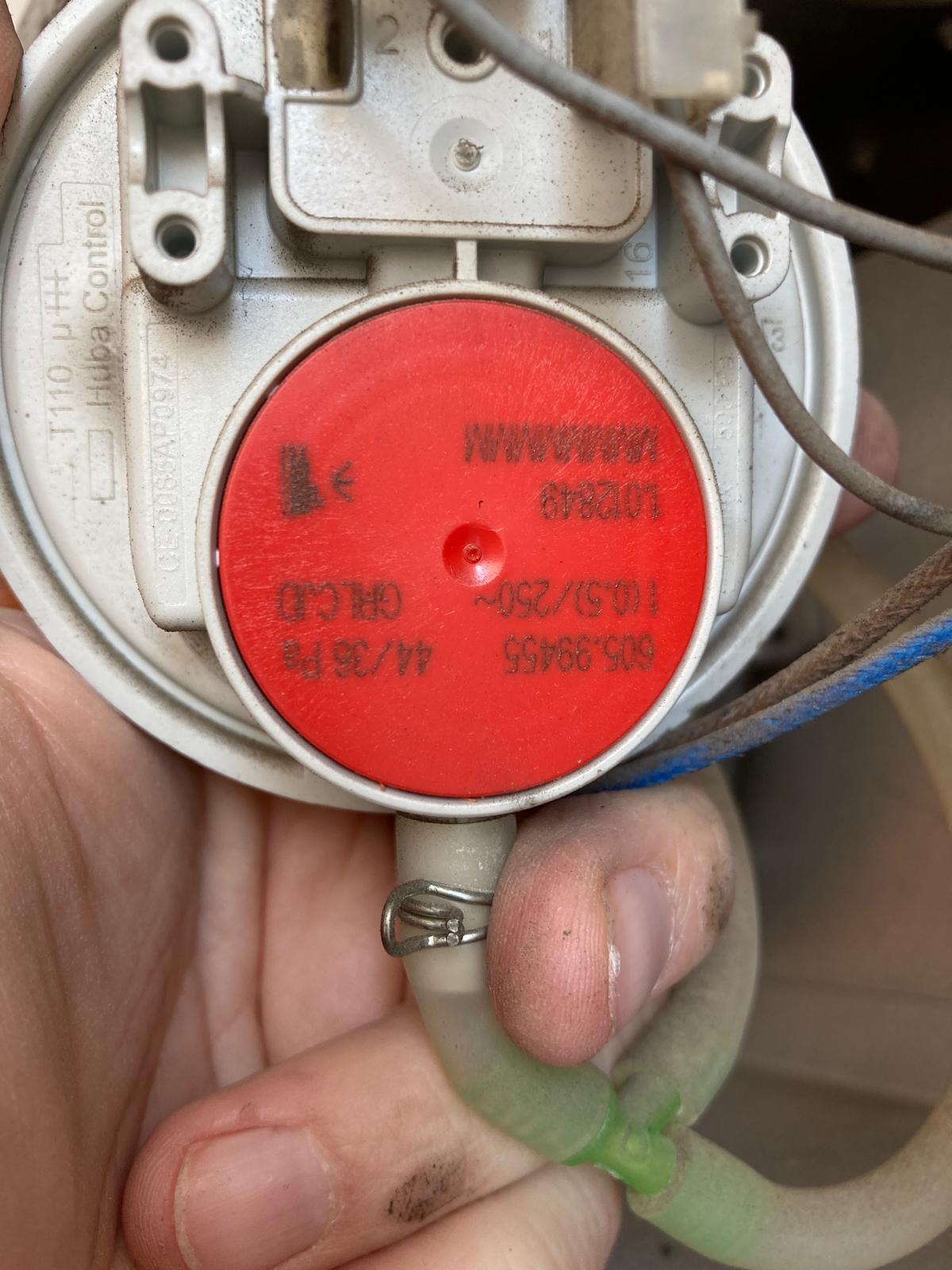 Detail zużytego presostatu Huba Control z czerwonym elementem, widoczne przewody i fragment dłoni. Urządzenie lekko zabrudzone, co sugeruje jego eksploatację.