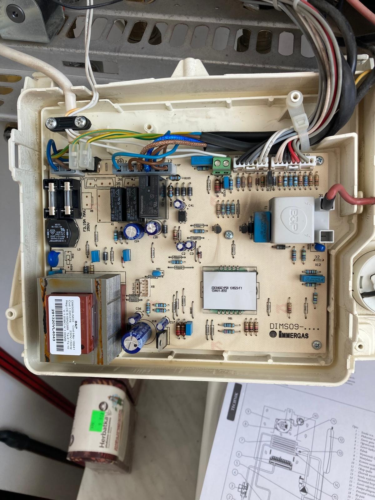 Płyta sterująca kotła gazowego Immergas DIMSO9 z widocznymi elementami elektronicznymi i przewodami. Obok instrukcja techniczna i opakowanie herbatki.