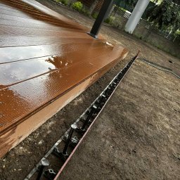 Greenera - Montaż brązowego tarasu kompozytowego na regulowanych wspornikach. Widoczne elementy konstrukcyjne i przygotowane podłoże.