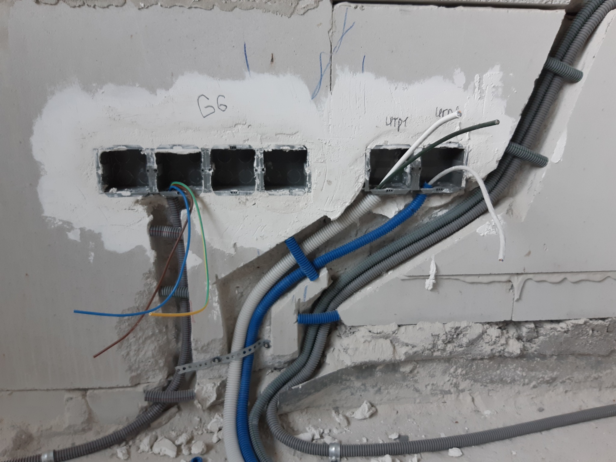 Elektryczne przewody w ścianie, w peszlach, prowadzone do puszek. Widoczne kable w kolorach: niebieski, żółty, zielony, brązowy i biały.