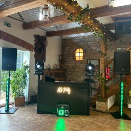 NAMAX EVENTS -DJ WODZIREJ FOTOBUDKA360 - Dekoracja sali z konsoletą DJ-ską, oświetleniem punktowym i kolumnami głośnikowymi, neon 'Let's Party', rustykalne elementy wystroju.