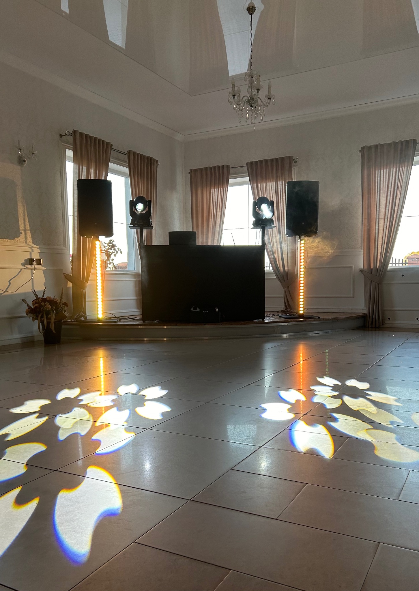 Sala balowa z parkietem, oświetleniem scenicznym i nagłośnieniem. Reflektory rzucają wzory na podłogę. Przygotowanie do imprezy.