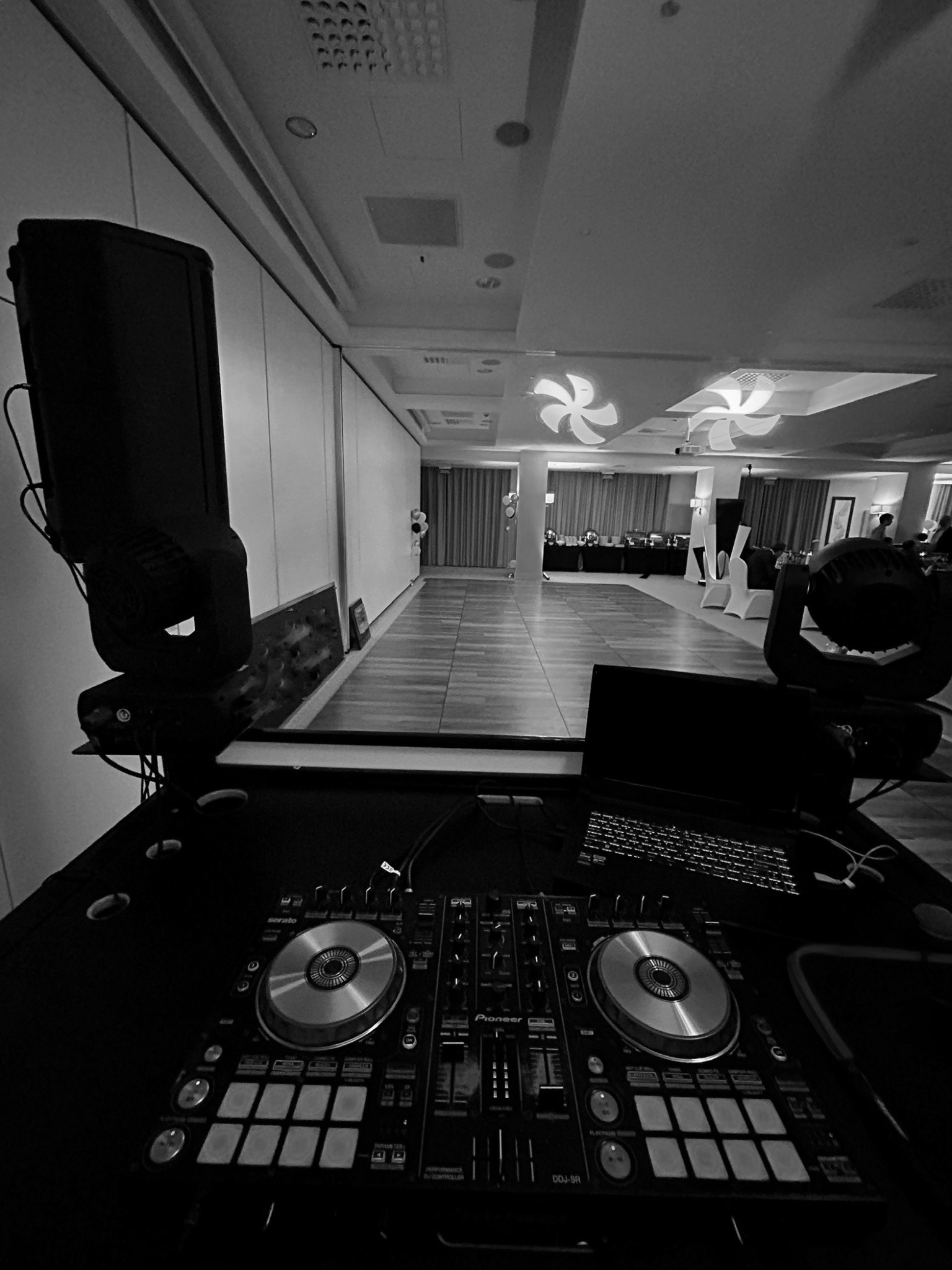 DJ-ski sprzęt Pioneer DJ DDJ-SR na stole, laptop, oświetlenie sceniczne w tle sali bankietowej w czerni i bieli. Przygotowania do imprezy.