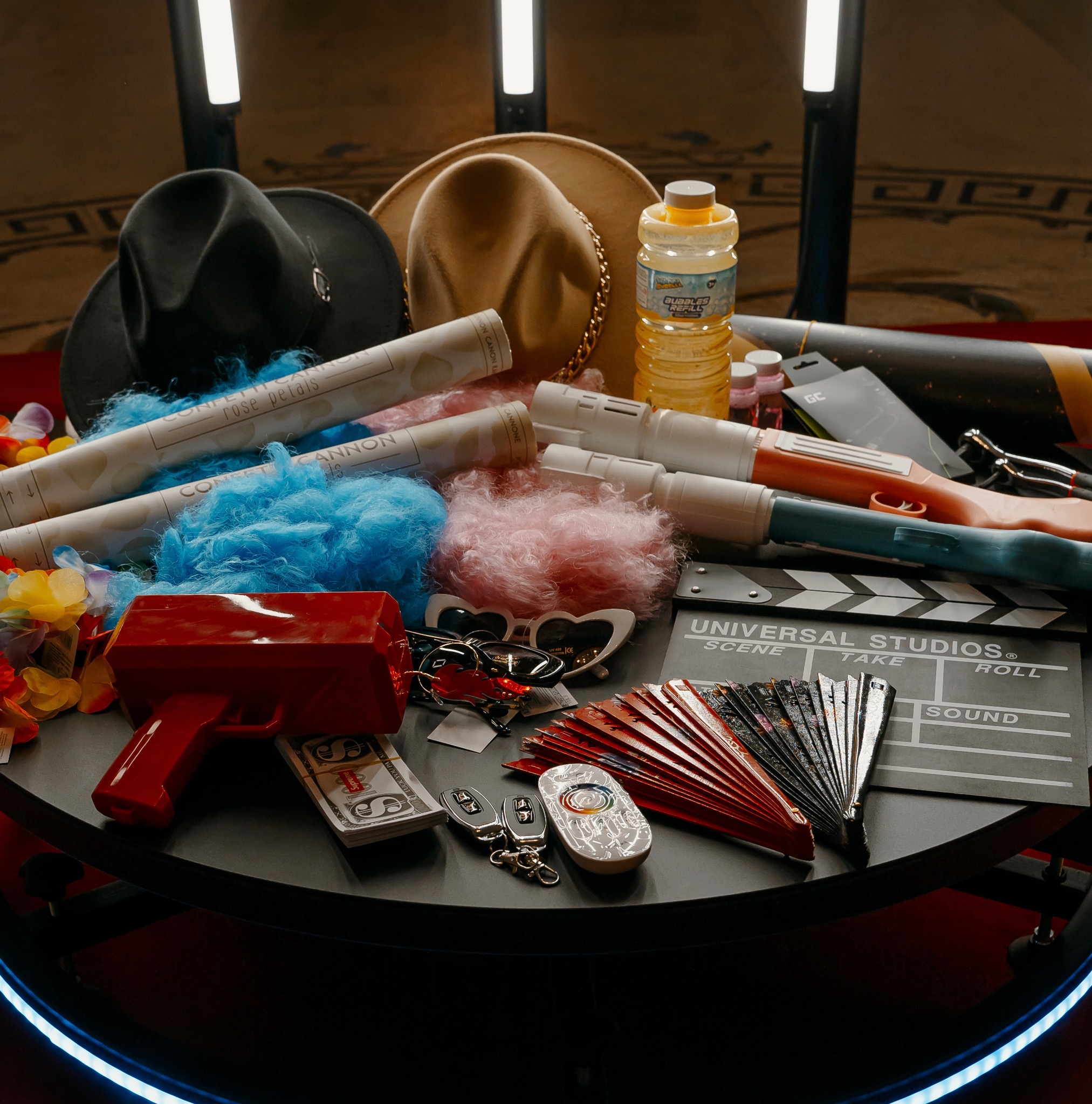 Rekwizyty na stole: kapelusze, konfetti, pistolety na bańki, klaps filmowy, wachlarze i rekwizyty pieniężne. Elementy scenografii imprezowej w zbliżeniu.