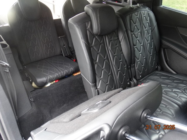 Wnętrze samochodu z czarnymi skórzanymi siedzeniami, widok z tyłu pojazdu. Fotele z geometrycznym wzorem przeszycia. Widoczne zagłówki i elementy mocowania.