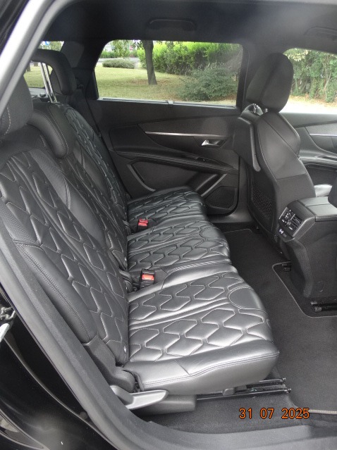 Wnętrze czarnego busa z trzema rzędami skórzanych, pikowanych siedzeń. Widok na tylne siedzenia z perspektywy pasażera. Czyste i zadbane wnętrze.