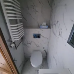 Biała toaleta z marmurowymi płytkami, grzejnikiem drabinkowym i dozownikiem mydła w nowoczesnej łazience po remoncie. Widok z góry, czyste wykończenie.