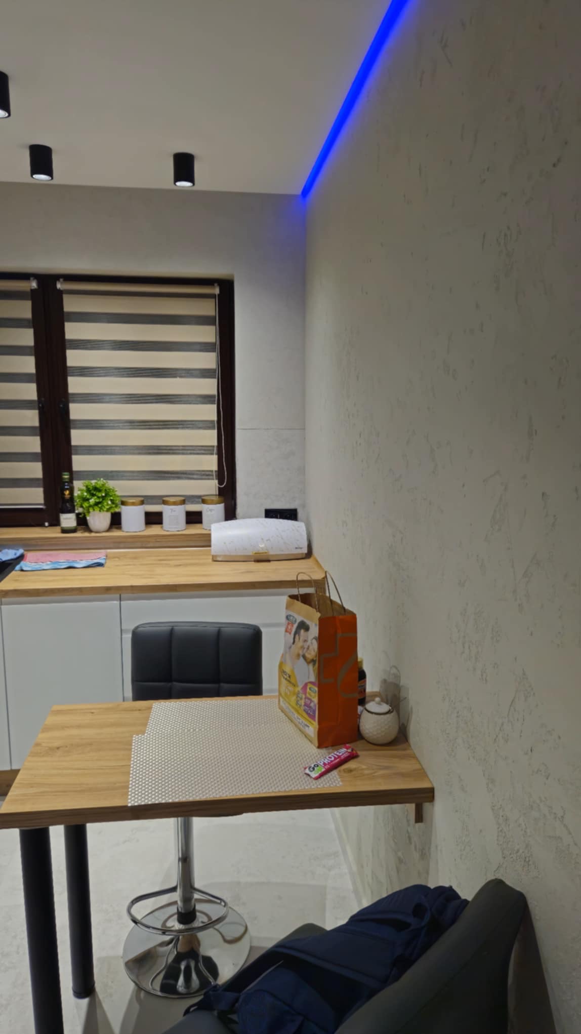 Nowoczesna kuchnia po remoncie: teksturowana ściana, podświetlenie LED, drewniany blat i rolety w oknie. Widok na odnowione wnętrze z bliska.