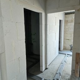 Biankowscy spolka z o.o. - Wnętrze w trakcie budowy: ściany z betonu komórkowego, instalacje elektryczne ułożone na podłodze, widoczne otwory drzwiowe i napisy na ścianach.