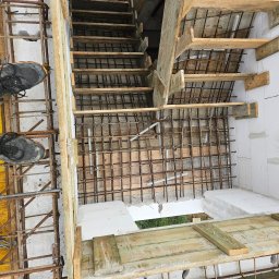 Biankowscy spolka z o.o. - Zbrojenie schodów i fundamentów z widocznymi stopami pracownika w obuwiu roboczym na żółtym szalunku. Ujęcie z góry ukazuje etap budowy.