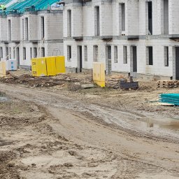 Biankowscy spolka z o.o. - Budowa szeregu domów z białego bloczka, z widocznymi numerami 6A, 6B, 6C, 6D. Częściowo zadaszone, z materiałami budowlanymi na błotnistym terenie.