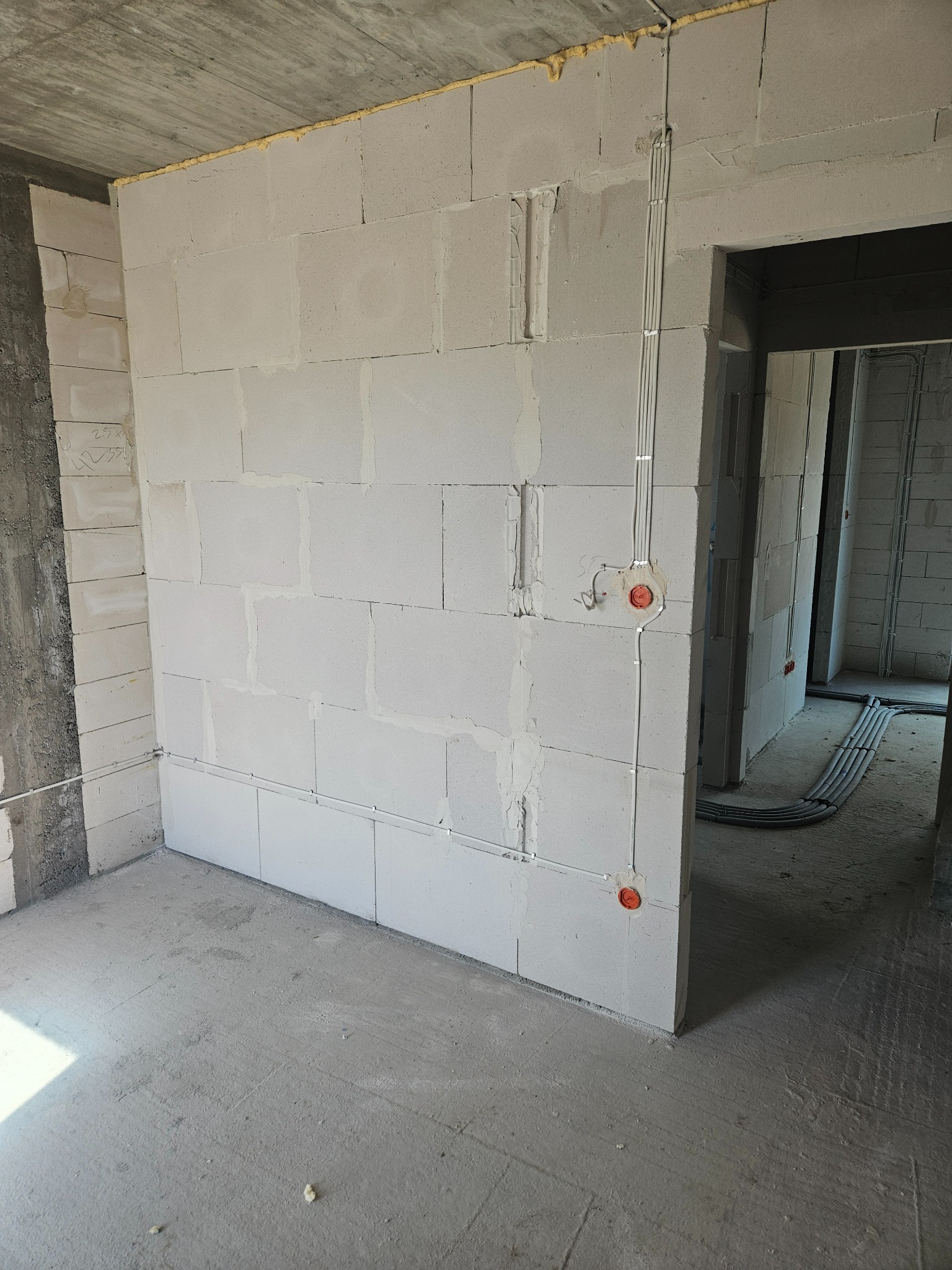 Wnętrze w stanie surowym: ściany z betonu komórkowego, instalacja elektryczna w peszlach, w tle widoczne kolejne pomieszczenia. Budowa domu na etapie instalacji.