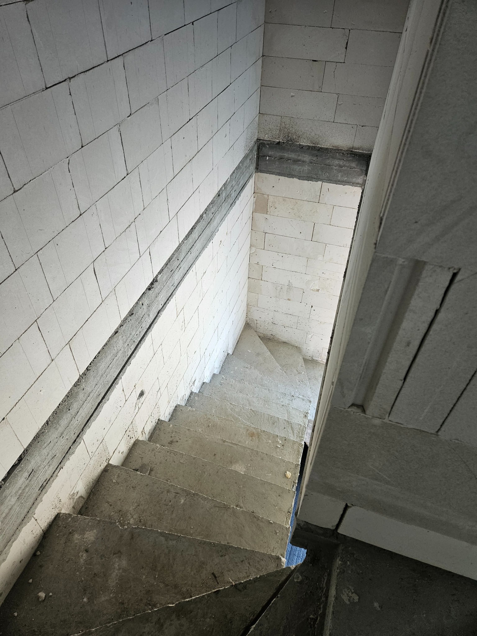 Wnętrze w trakcie budowy z betonowymi schodami i ścianami z białych bloczków, widok z góry, szare fugi, surowy stan, budowa domu.