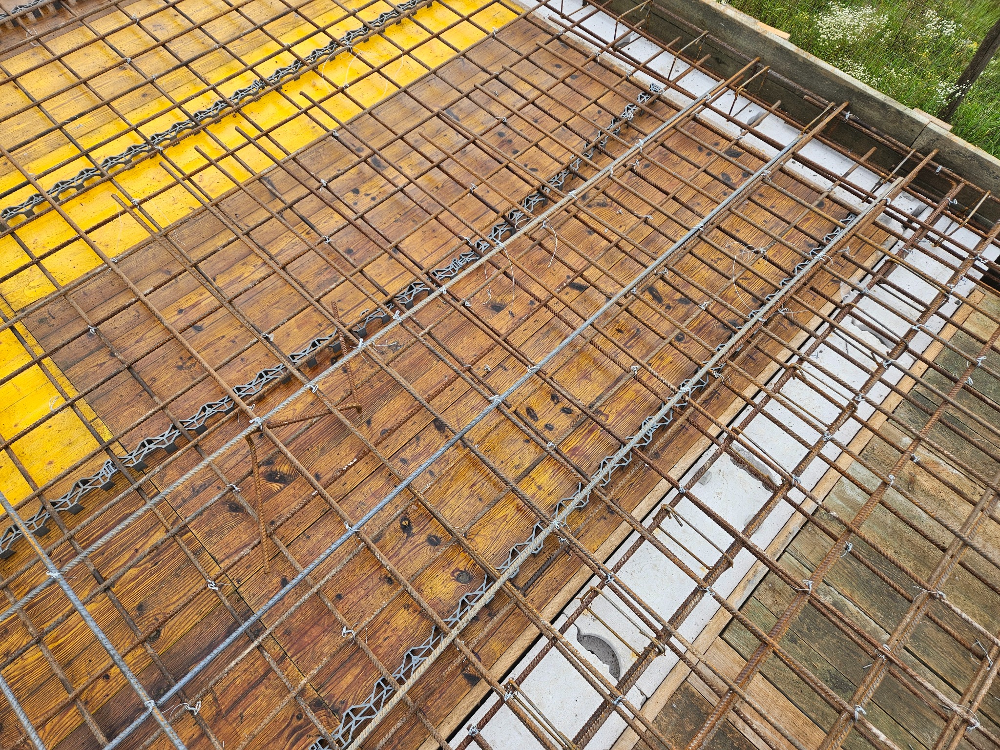 Zbrojenie płyty fundamentowej na deskowaniu z widocznymi elementami dystansowymi i otworami instalacyjnymi, wykonane przed zalaniem betonem.