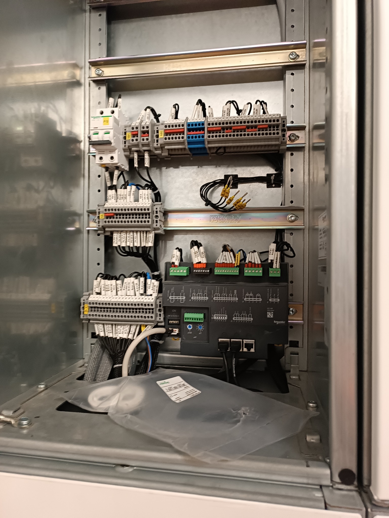 Wnętrze szafy sterowniczej z widocznymi elementami instalacji elektrycznej: bezpieczniki, listwy zaciskowe, kable z oznaczeniami i sterownik. Widoczne złącza ethernet.